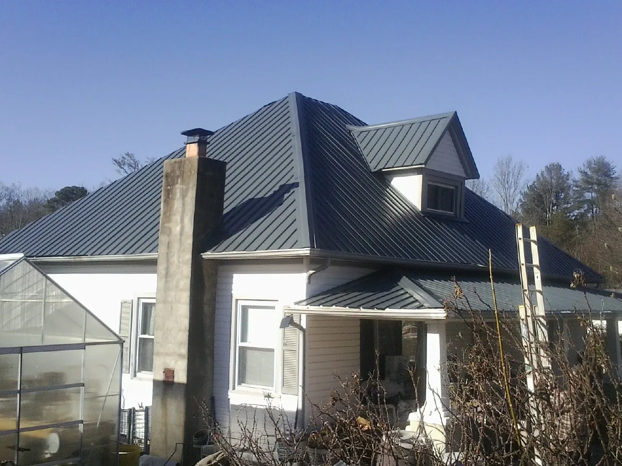 Dark blue standing seam metal roof on a white farmhouse with dormer — Slate & Tile Roof Repair by Roofing Brothers in Norman