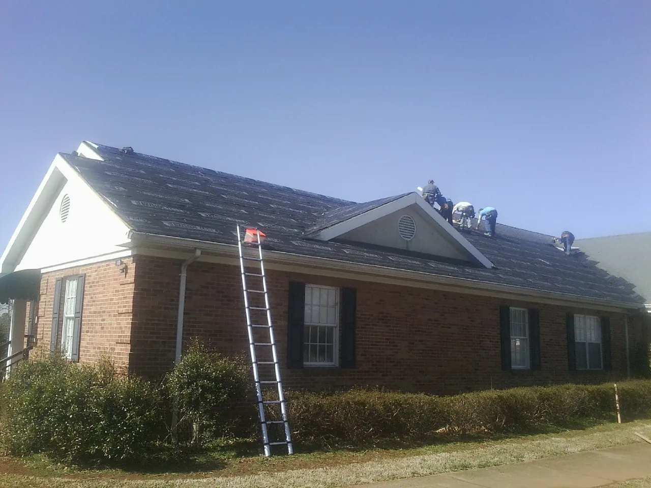 Crew tearing shingles off a brick ranch roof with a ladder set — Metal Roof Repair work by our crew in Norman