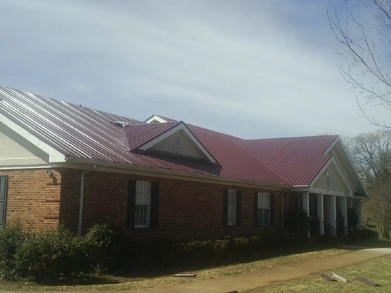 Red metal roof with gabled entries on a long brick building, from a Hail Damage Roof Repair job in Norman