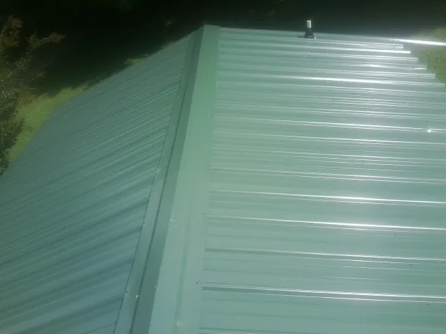 New green metal panels meeting at the ridge of a roof — Flat Roof Repair work by our crew in Norman